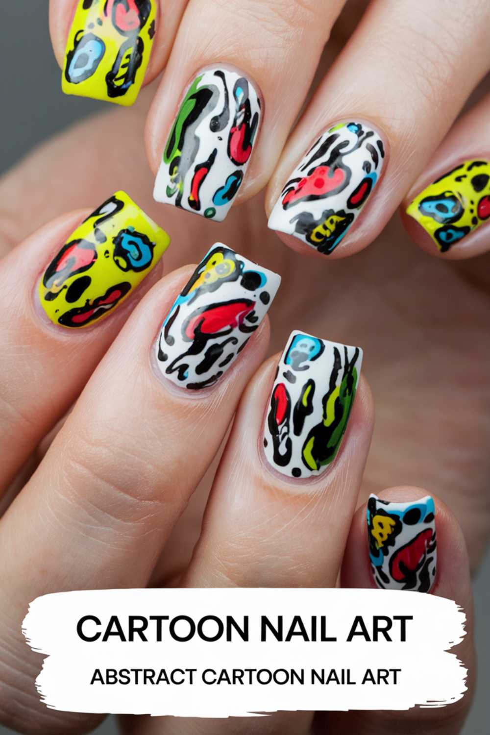 Close-up of a hand with cartoon nail art designs. The nails showcase vibrant abstract patterns with splashes of yellow, blue, red, and black on a white background. Text below reads, CARTOON NAIL ART - ABSTRACT CARTOON NAIL ART.