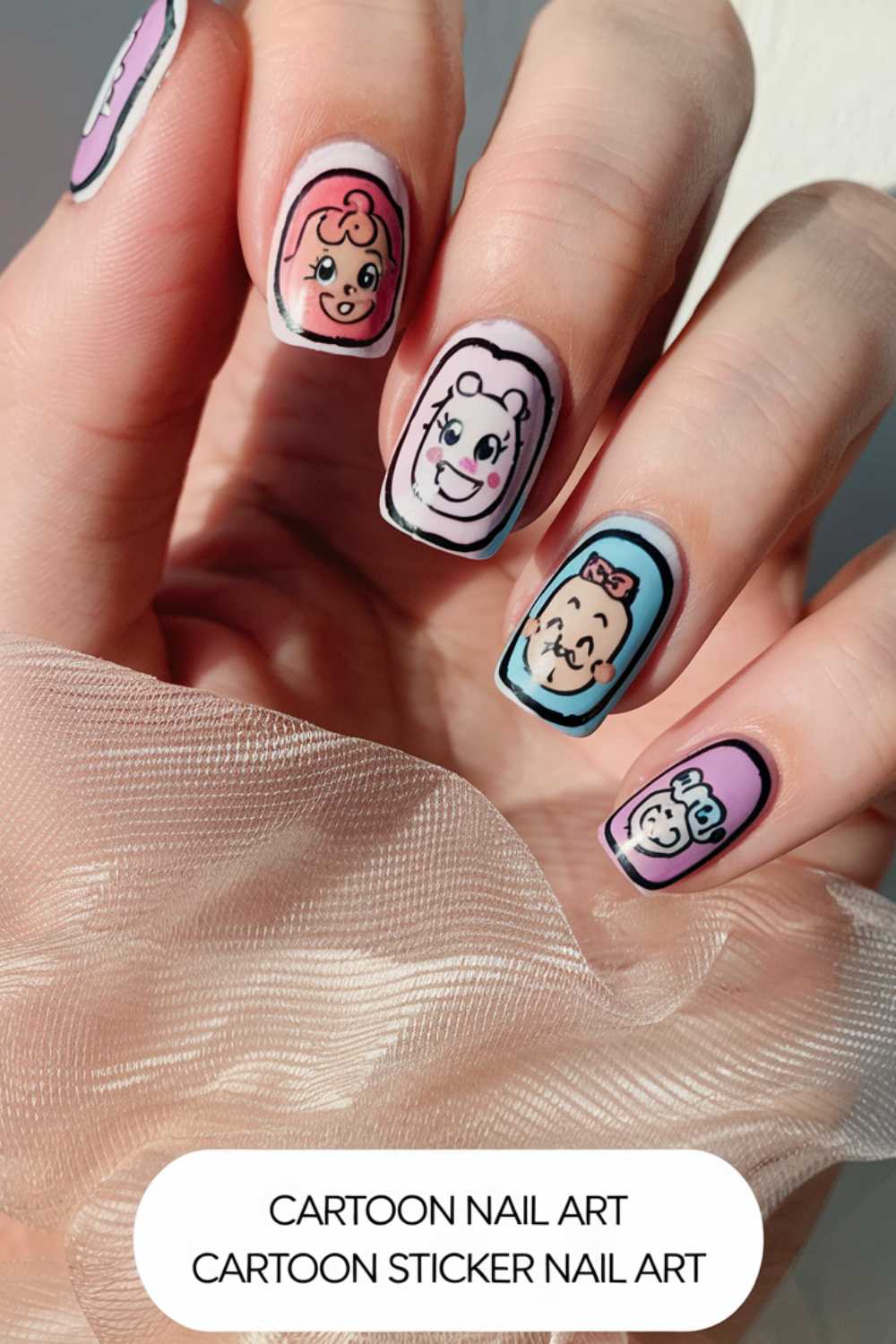 A close-up of a hand showcases vibrant cartoon nail art designs. Each fingernail flaunts a colorful, outlined character sticker, set against a pink background. The hand is partly veiled by sheer fabric.