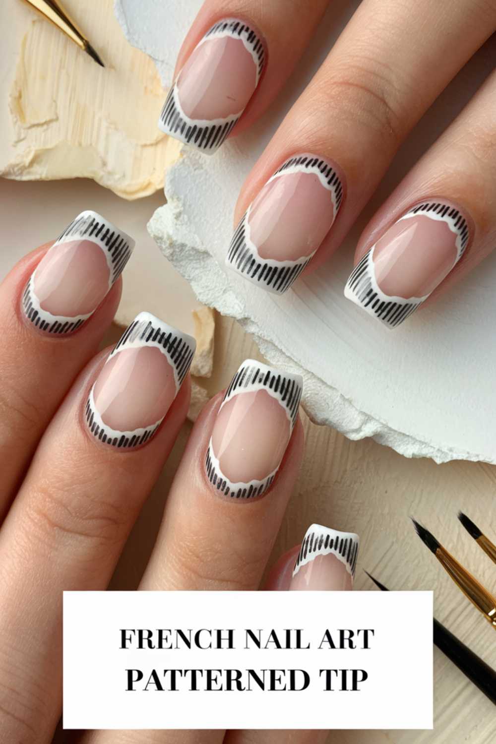 A hand displays a French manicure with patterned tips. The nails have a natural base with white and black striped tips. The text at the bottom reads French Nail Art Patterned Tip. Brushes and decorative materials are visible in the background.